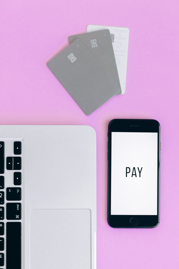 Vue de dessus d’une configuration de paiement mobile avec un smartphone, des cartes bancaires et un ordinateur portable sur un fond rose.